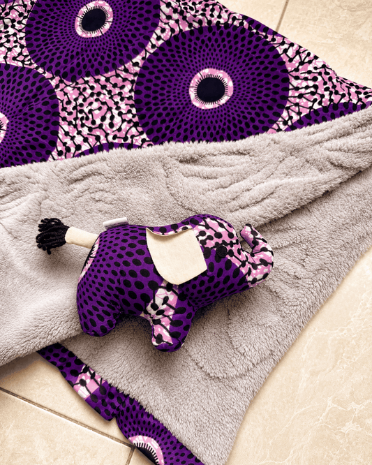Purple and pink patterned dog toy on a gray blanket with a purple and pink circular design in the background.