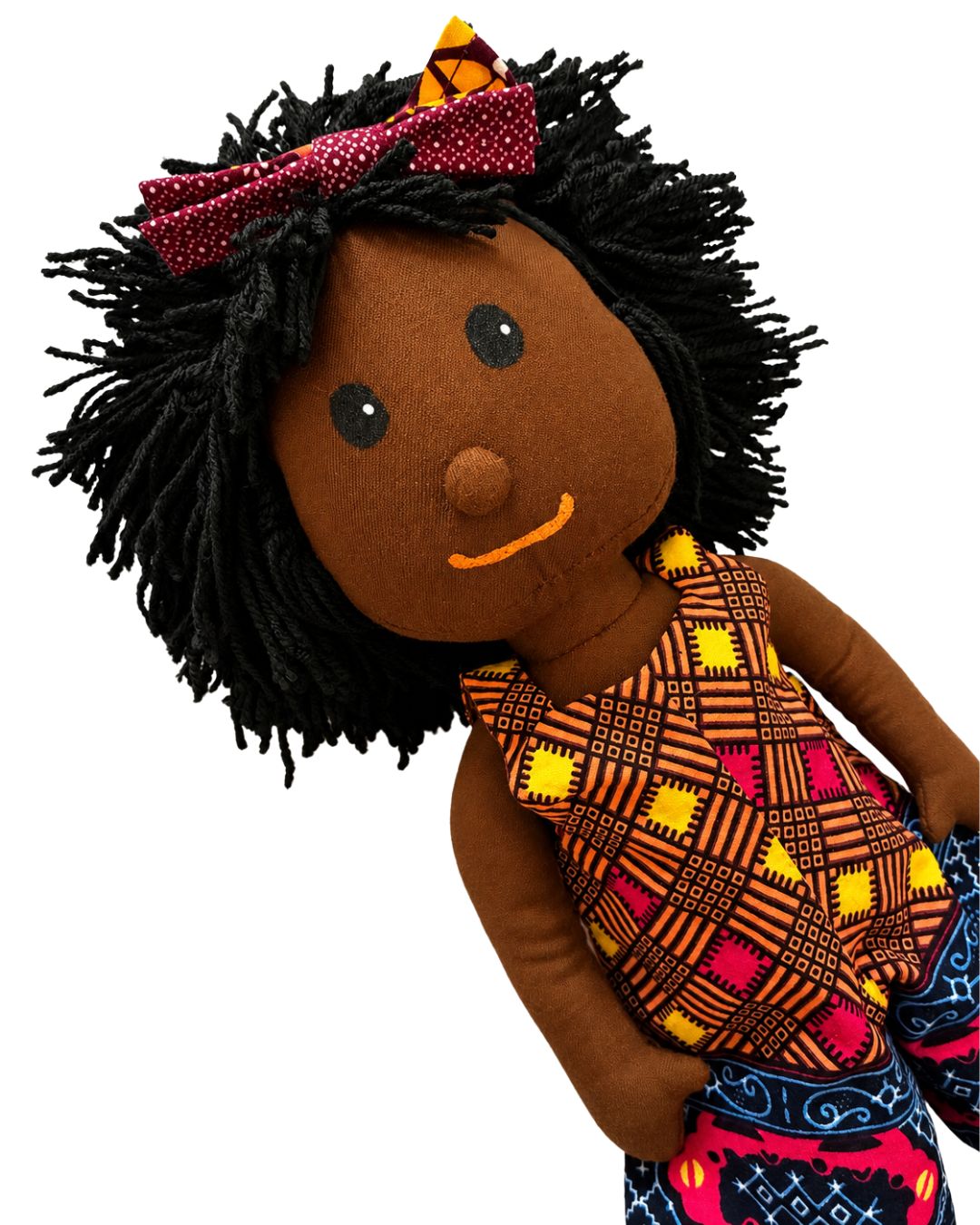 A handmade African-style cloth doll with black yarn hair, a red patterned bow, and a colorful geometric-patterned dress, shown against a plain white background.