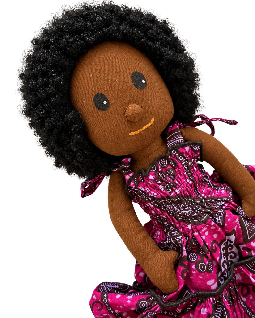 A handmade fabric doll with dark brown felt skin, black curly hair, and a pink patterned dress, shown against a plain white background.