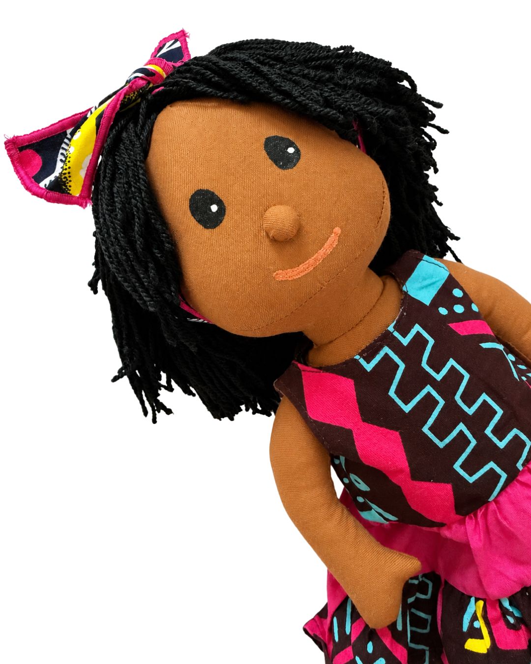 A handmade fabric doll with brown skin, black yarn hair, and a colorful patterned dress and hair bow, shown against a plain white background.