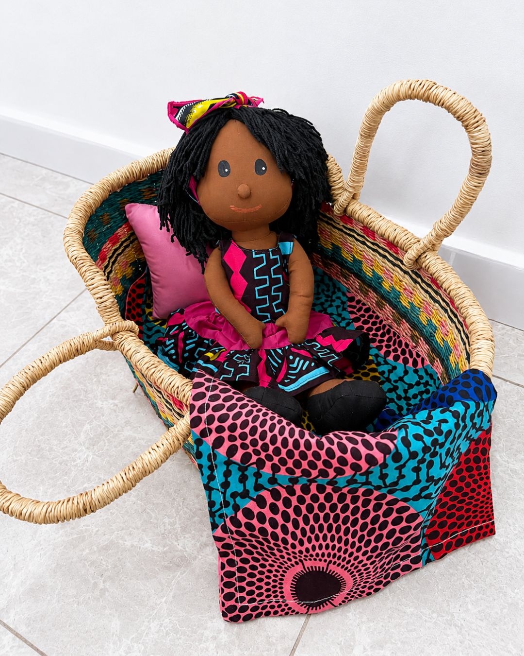 african doll in a handwoven dolls basket with african print bedding set on a white background