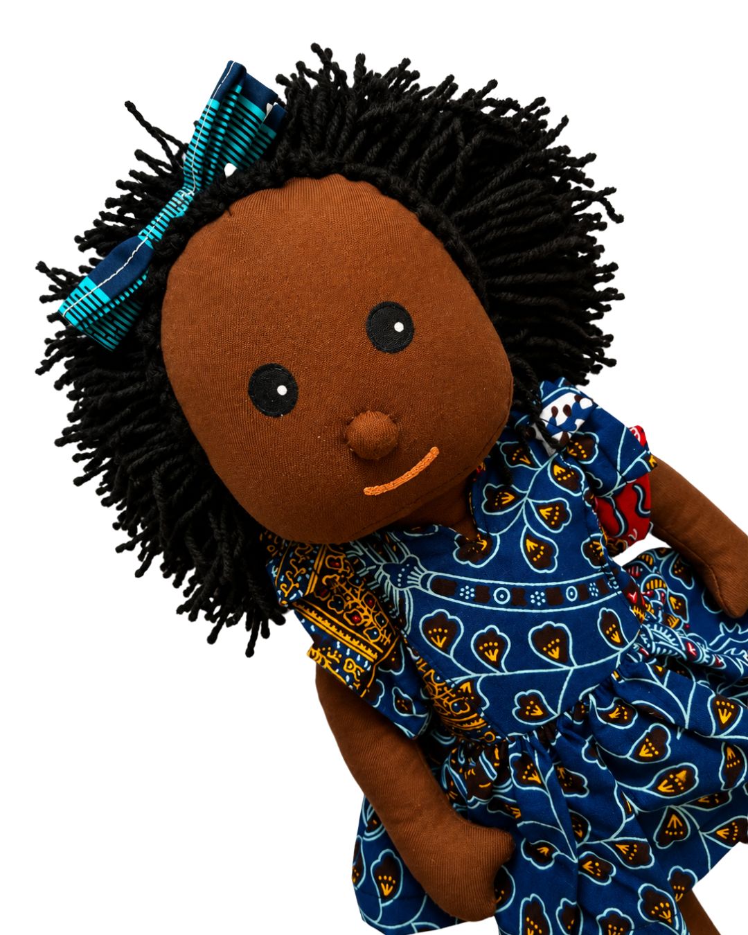 A handmade African American doll with black yarn hair styled in a messy bun with a blue patterned bow, wearing a blue patterned dress, isolated on a white background.