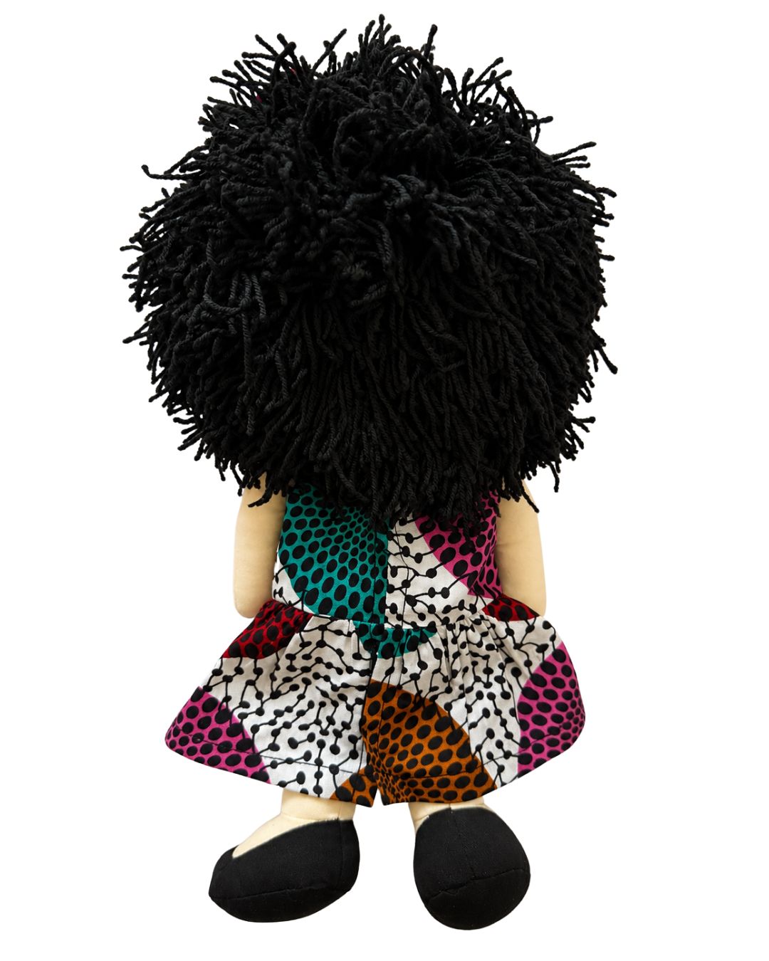 A plush doll viewed from the back, featuring a large black shaggy afro wig, beige skin-toned arms and legs, and a colorful patchwork-patterned dress with black shoes.