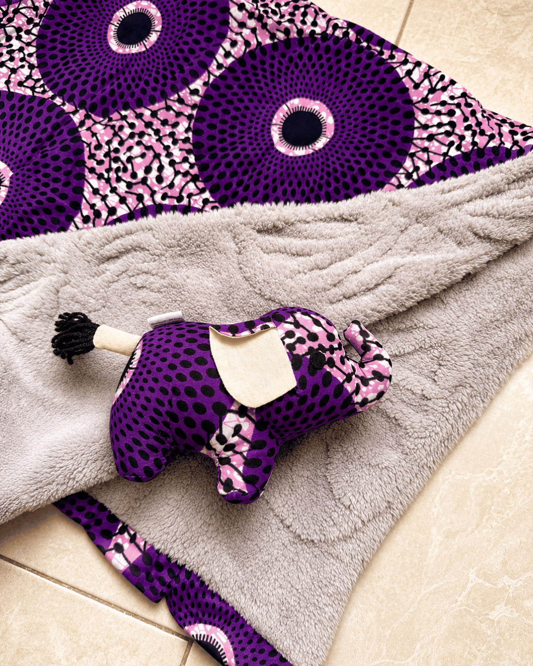 Purple and pink patterned dog toy on a gray blanket with a purple and pink circular design in the background.