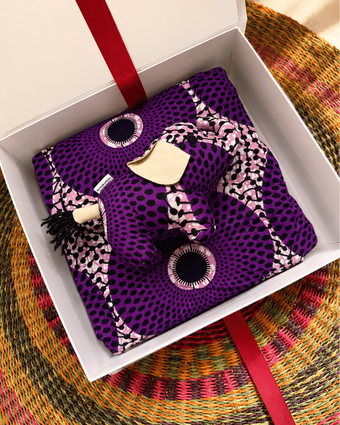 Purple patterned fabric with a decorative button in a white box on a colorful woven surface.