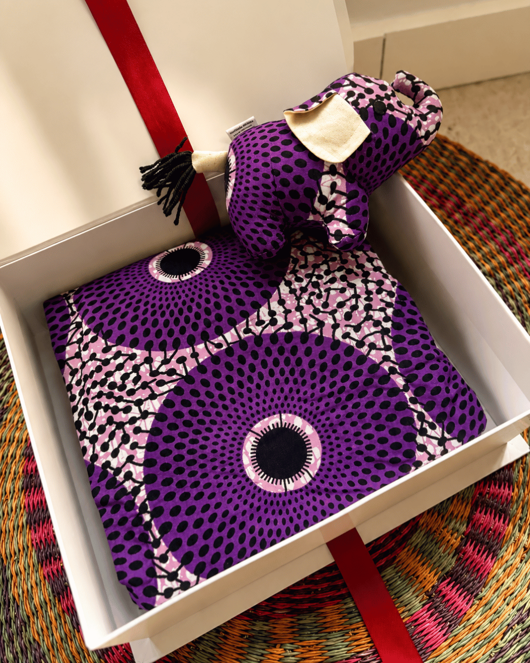 Purple patterned fabric with a decorative bow in a white box on a colorful rug.