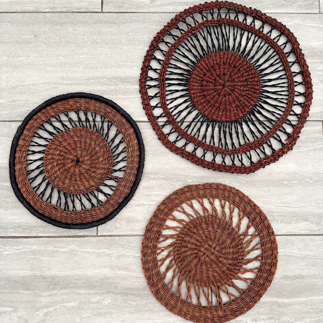 Three woven wall baskets with black and brown patterns on a wooden surface