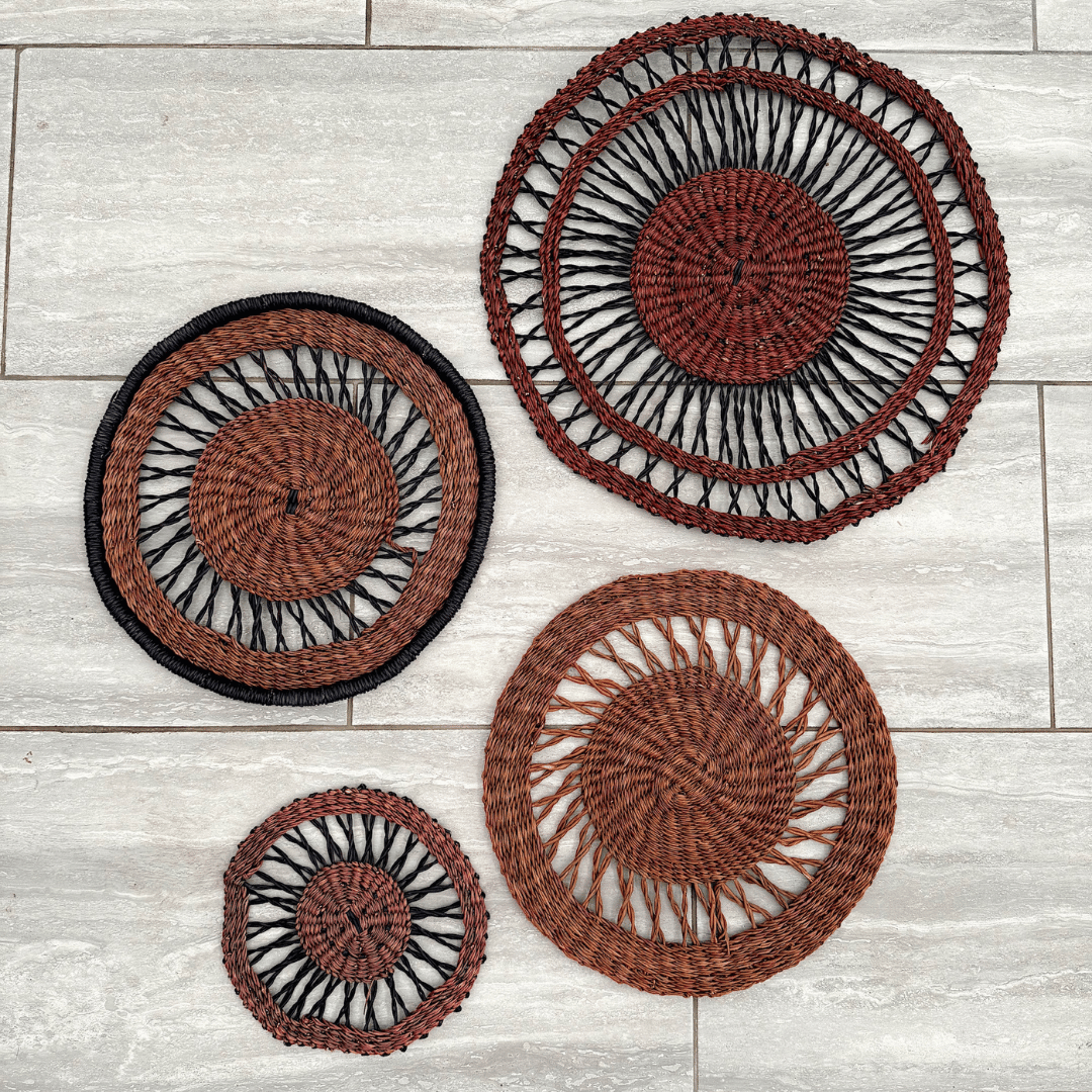 Set of four woven wall baskets with black and brown design on a light wooden surface